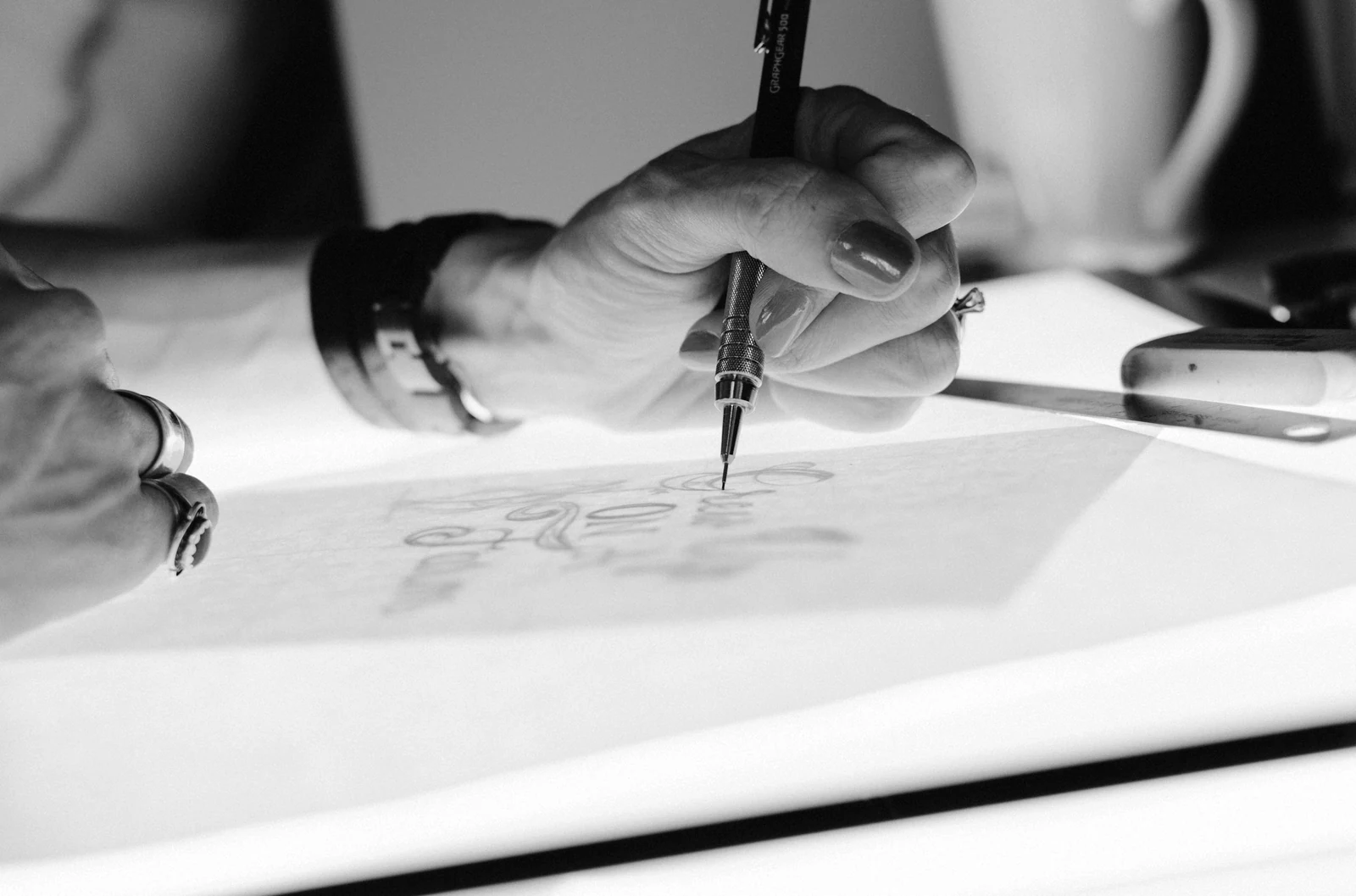 person lettering on tracing paper using mechanical pencil. Photograph accompanying Velaharra’s artist commission budget guide.
