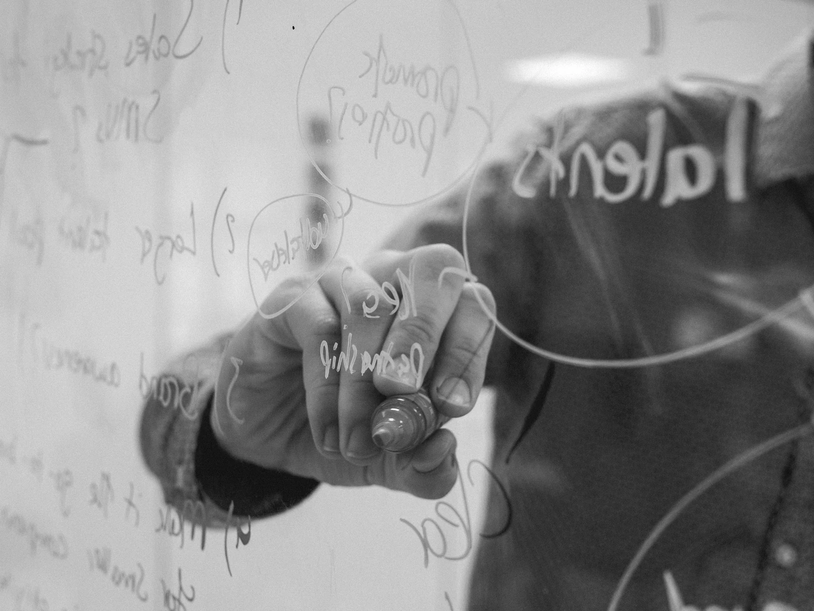 person writing on glass whiteboard with diagrams. Photograph accompanying Velaharra’s cultural advisor Austin guide.